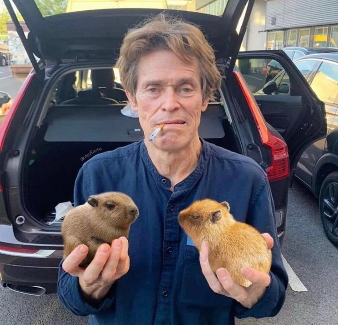 Willem Dafoe with a cigarette in his mouth and a baby capybara in each hand